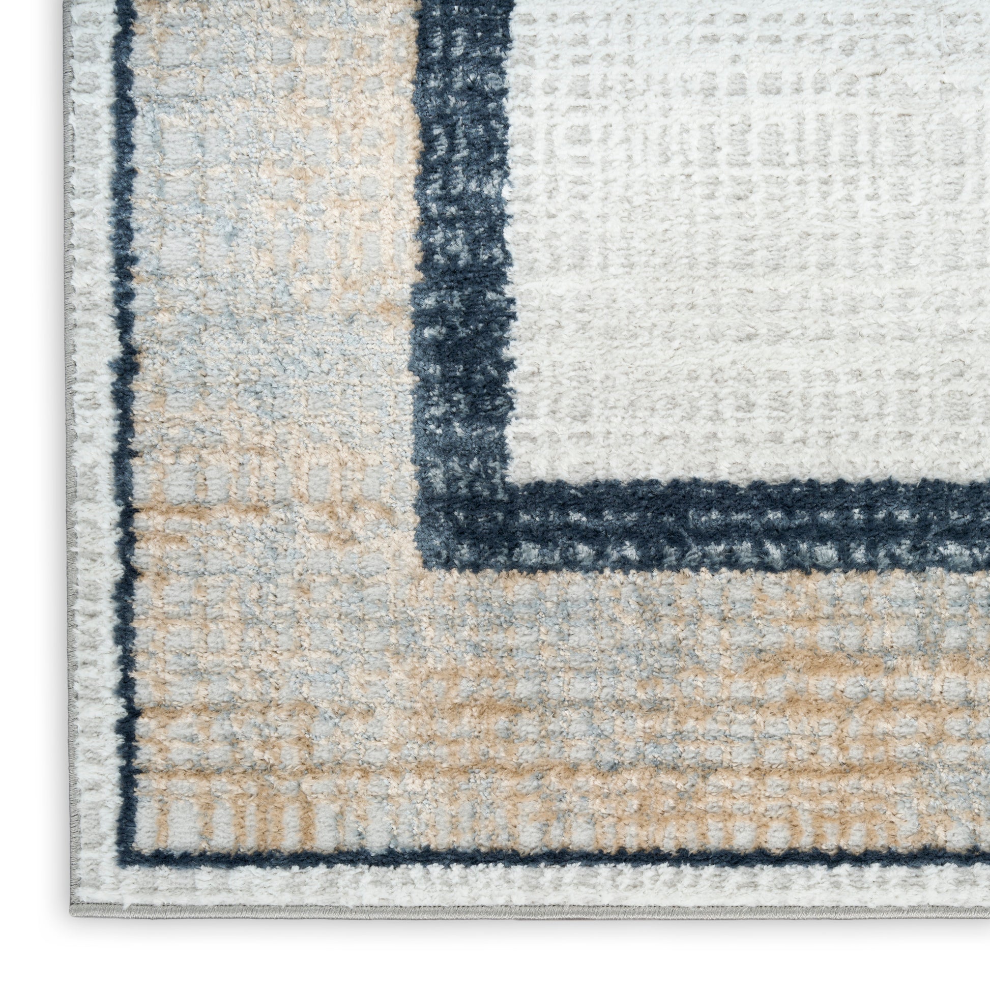 Close-up of a tufted geometric rug with cream, beige, light blue blocks and dark navy borders; soft pile.