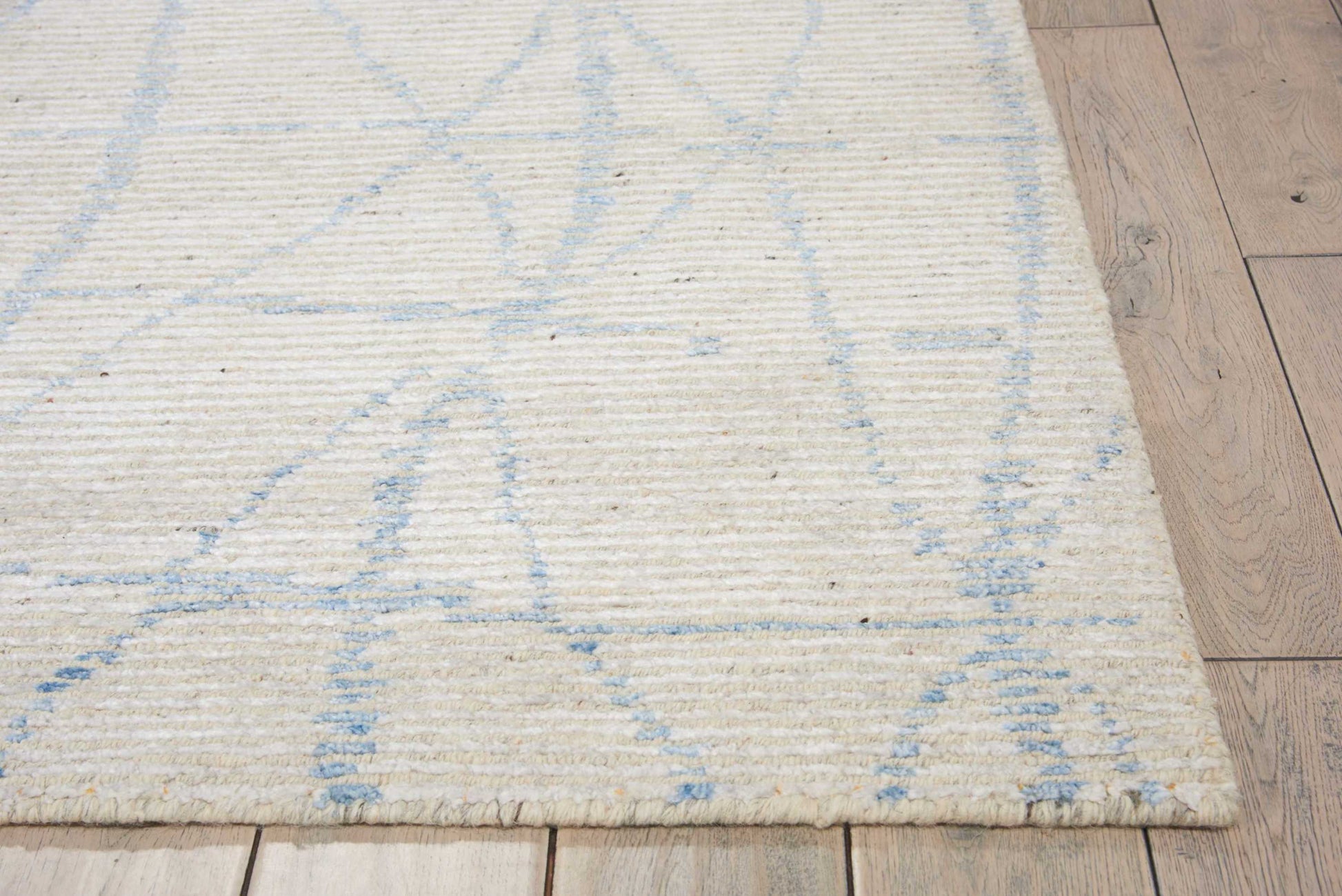Ivory flatweave rug with pale blue geometric lines on light wood floor.