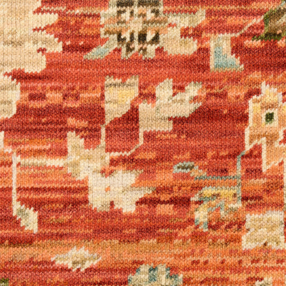 Close-up of a woven area rug in warm red-orange tones with beige and pale blue abstract floral patterns.