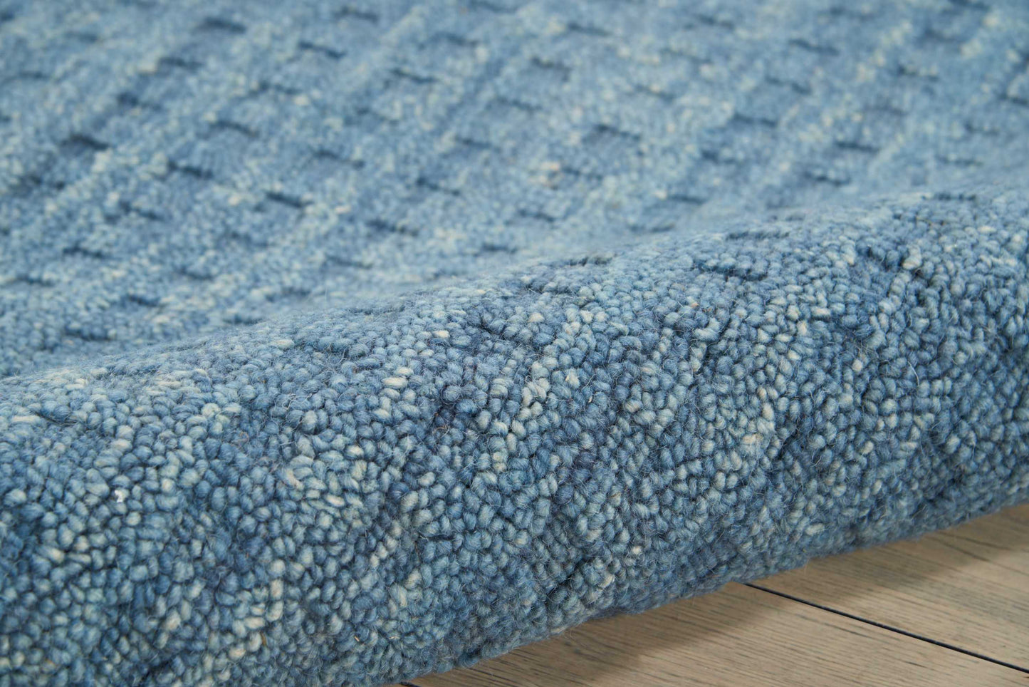 Blue shaggy rug with dense loop-pile, plush texture, edge resting on light wood floor.