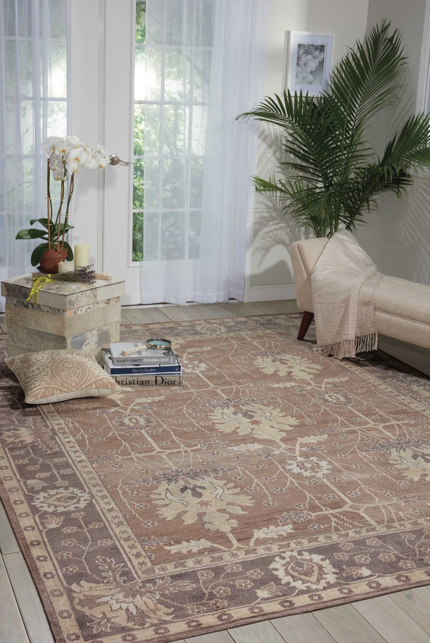 Cozy living room with cream chaise, ornate beige rug, tall potted plant, orchid on stone side table, glass doors in back.