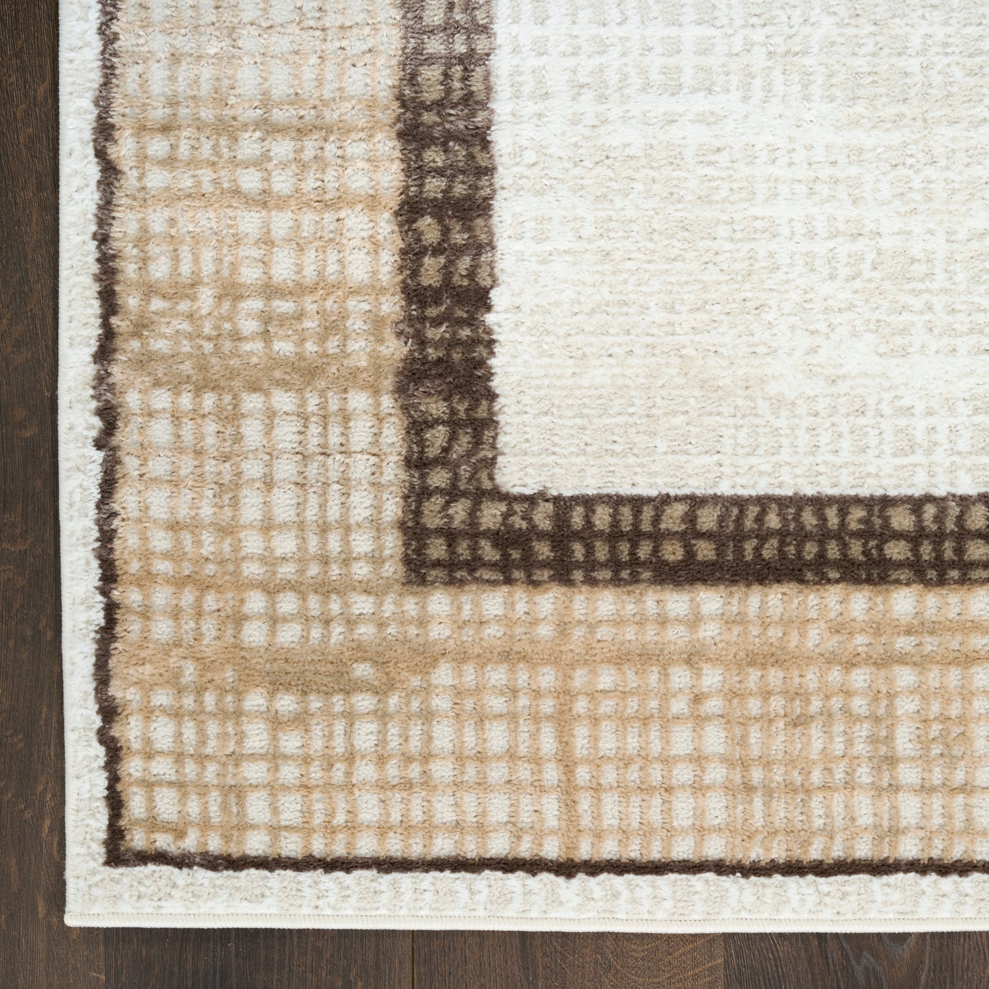 Tan & cream tufted area rug with dark brown border and geometric grid pattern, corner view on wood floor.