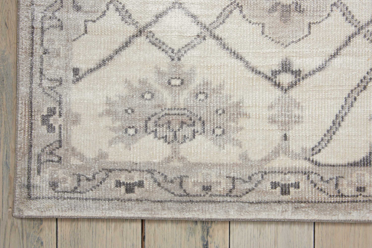 Cream and gray oriental area rug with diamond lattice, floral medallion, and geometric border on a wooden floor.
