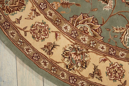 Round oriental rug with teal field and cream-beige border featuring floral motifs on a light wood floor.