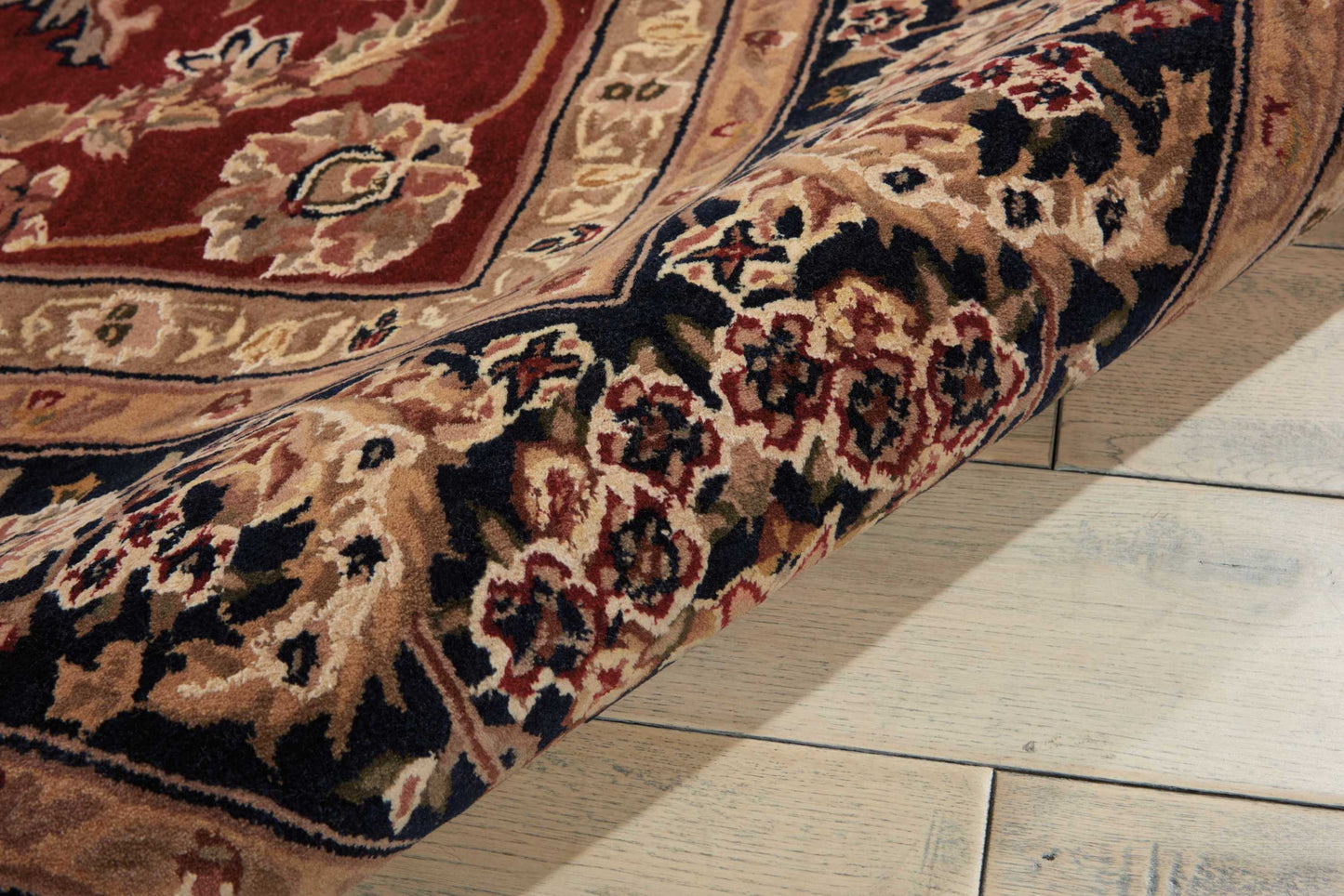 Close-up of ornate red and beige oriental rug with floral border, partially rolled on light wood floor.