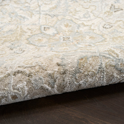 Close-up of a cream oriental rug with grey-blue floral pattern, folded edge on a dark wooden floor.