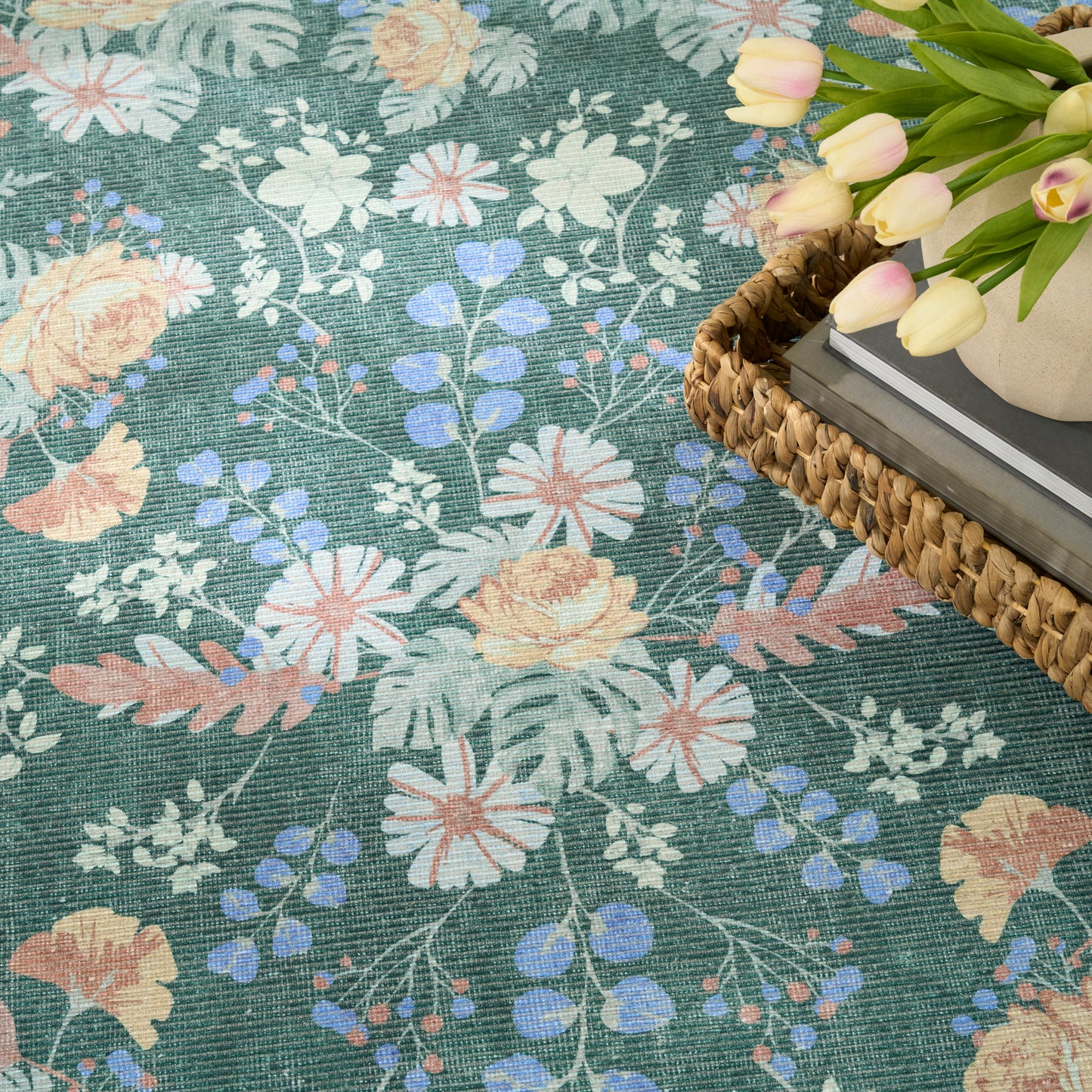 Teal floral woven rug (4' x 6') with peach, white and blue blossoms; wicker basket & pale tulips and a stack of books.