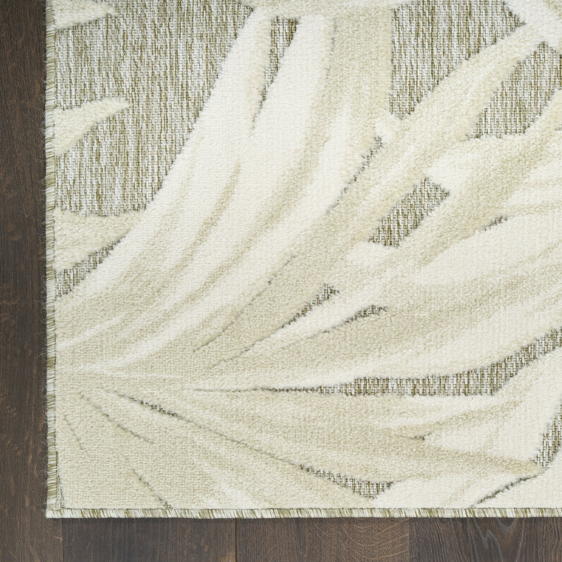 Cream ivory palm-leaf patterned rug with soft textured pile and fringed edge on dark wood floor.