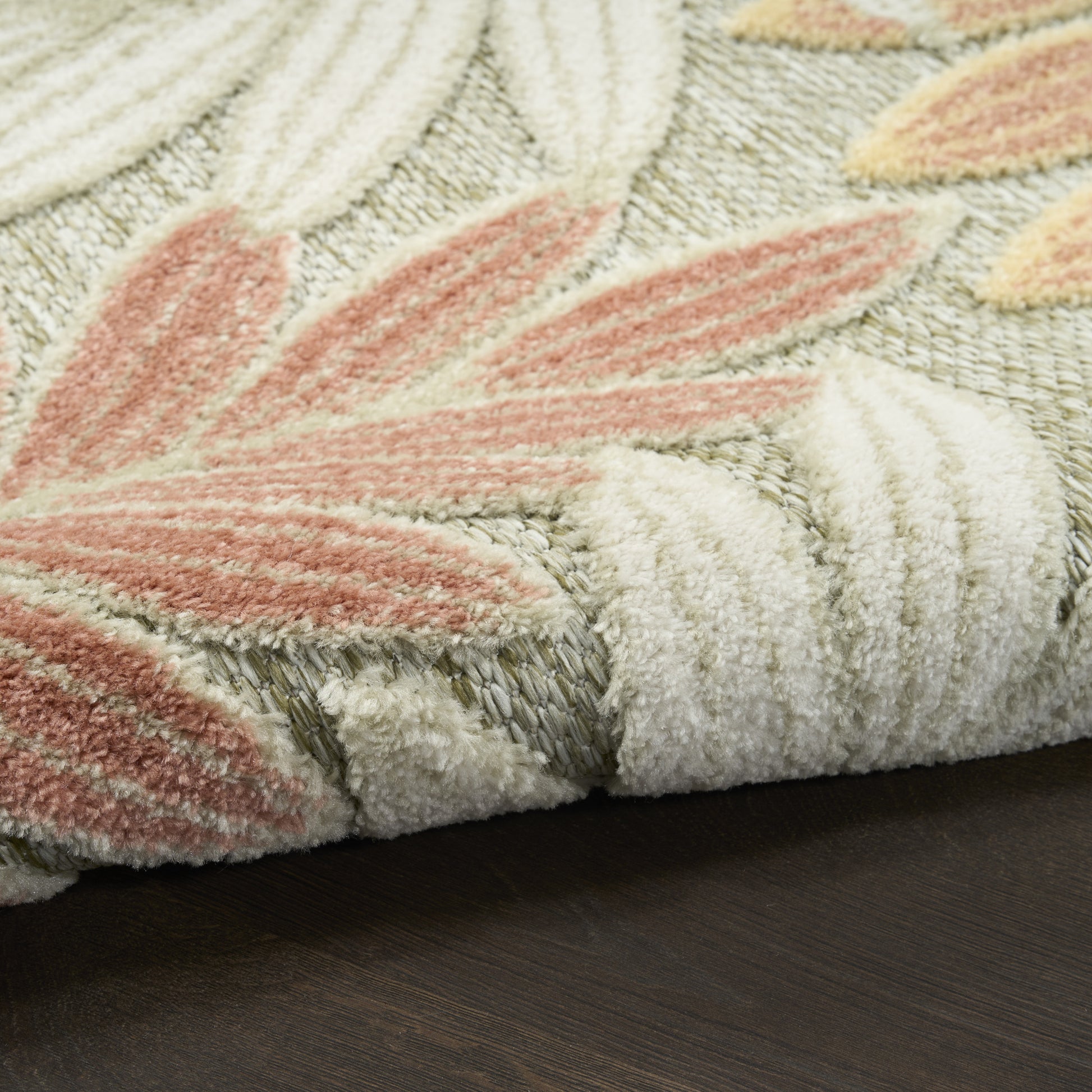 Close-up of a cream shag rug with peach-pink leaf motifs on ivory, folded edge on dark wood floor.
