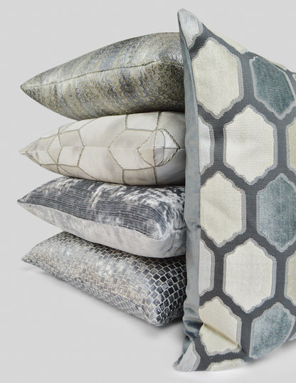 Stack of four decorative throw pillows in grey-blue tones with geometric hexagon patterns and textured finishes.