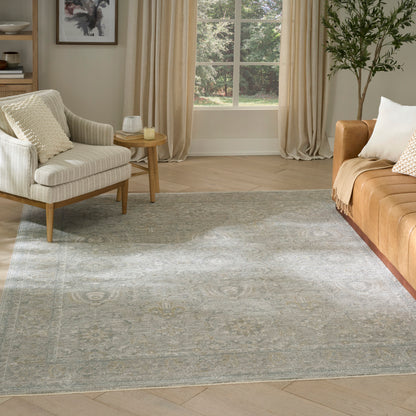 Blue-gray patterned area rug in a modern living room with cream armchair, tan leather sofa, and wooden side table.