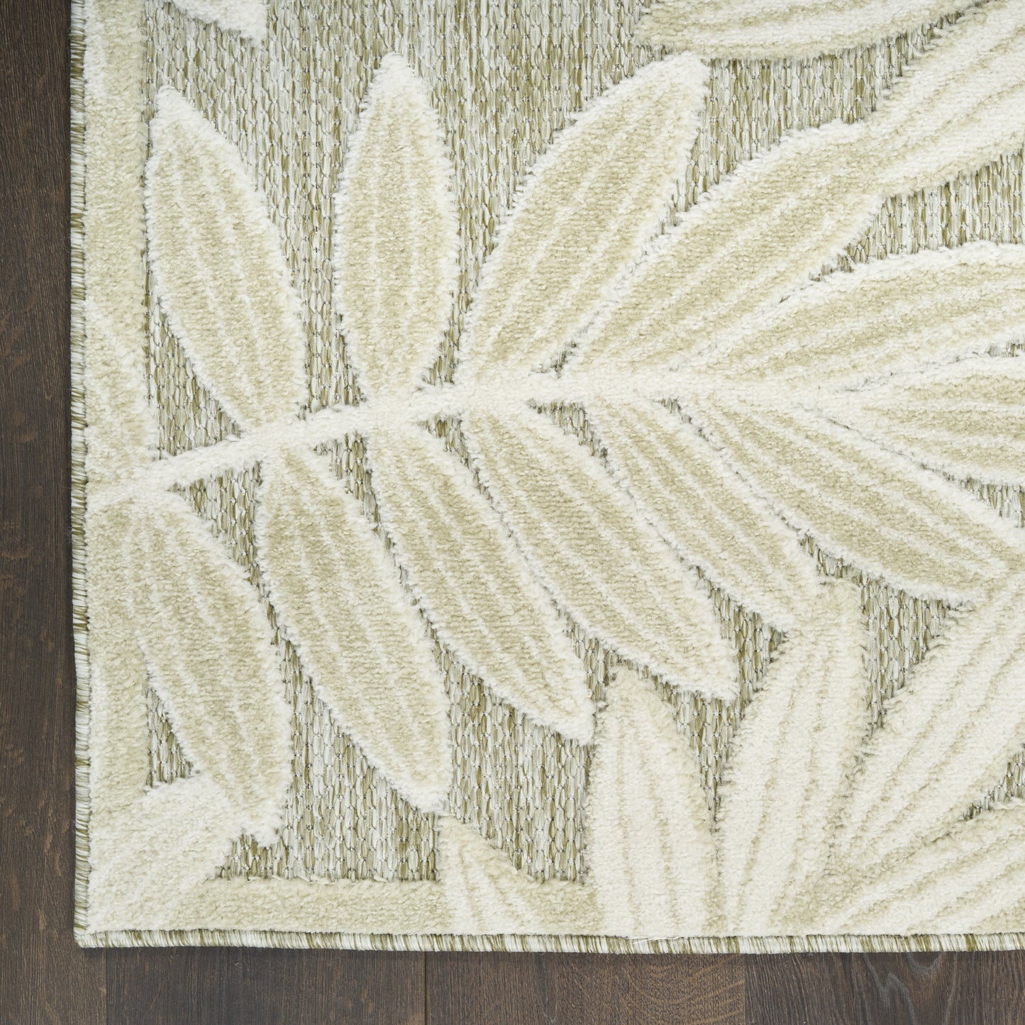 Cream leaf-pattern area rug with large ivory fronds on textured taupe background, bordered, on dark wood floor.