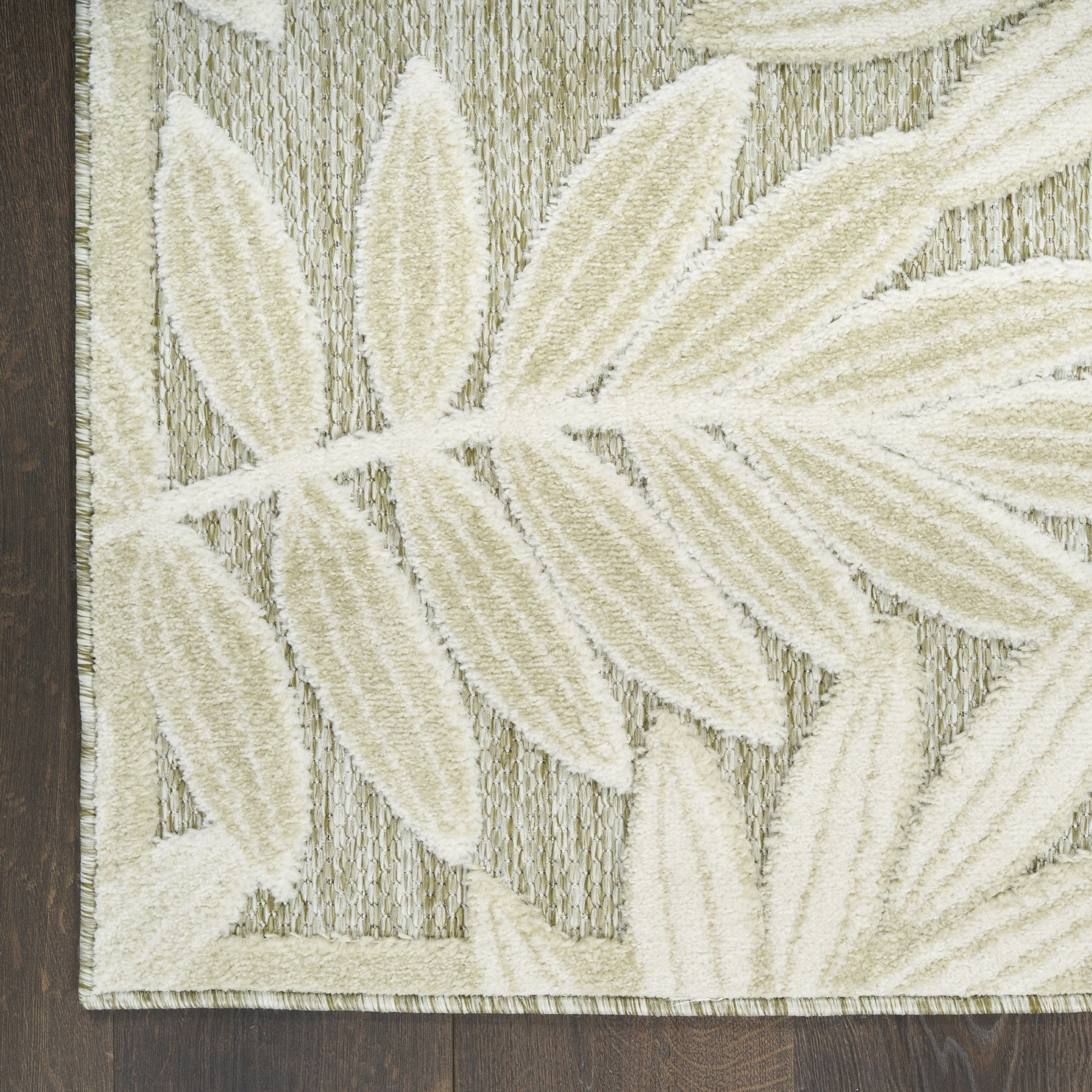 Cream leaf-pattern area rug with large ivory fronds on textured taupe background, bordered, on dark wood floor.