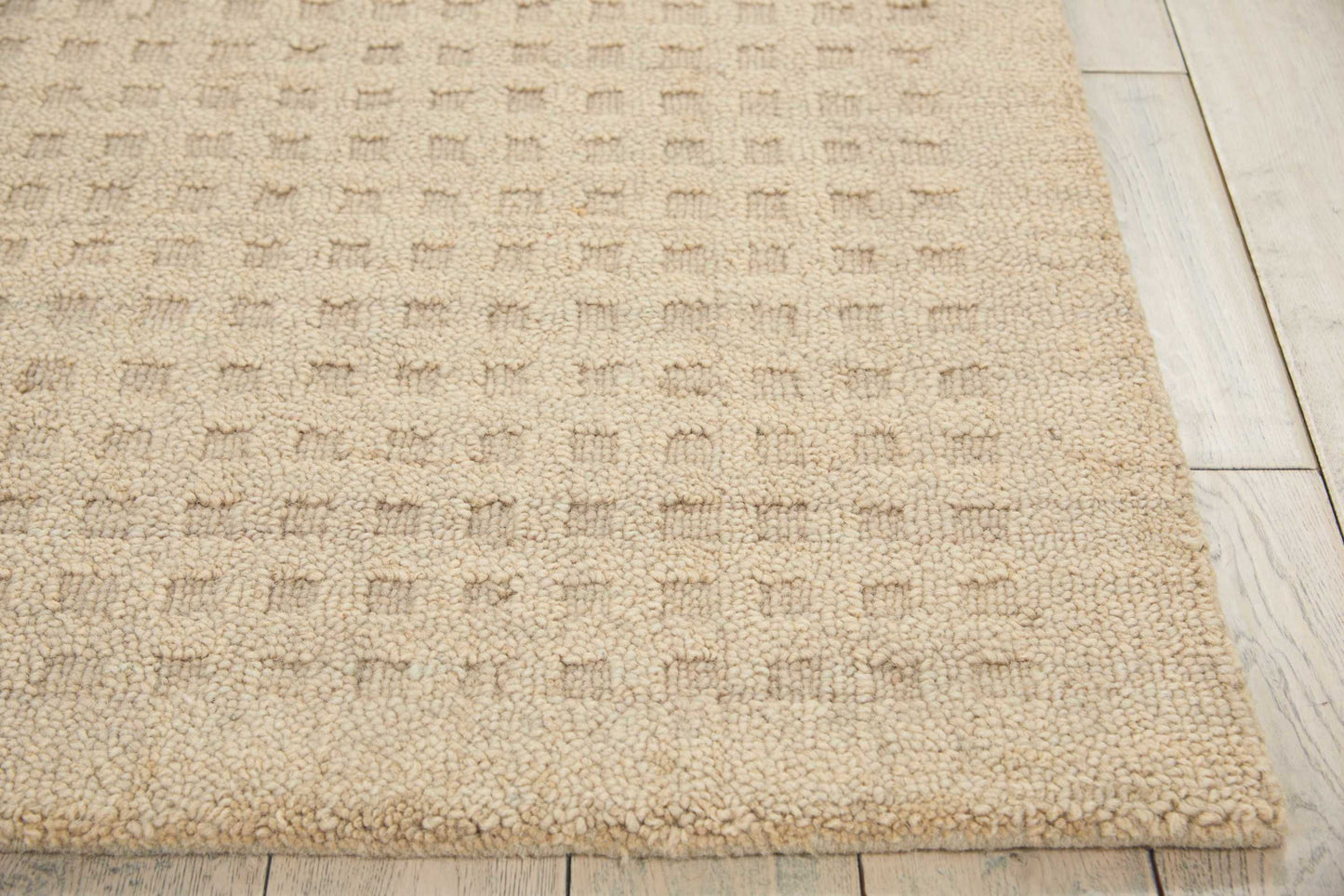Beige textured rug with a subtle square pattern and thick boucle pile on light wood flooring.