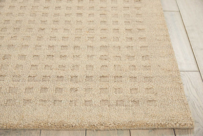 Beige textured rug with a subtle square pattern and thick boucle pile on light wood flooring.