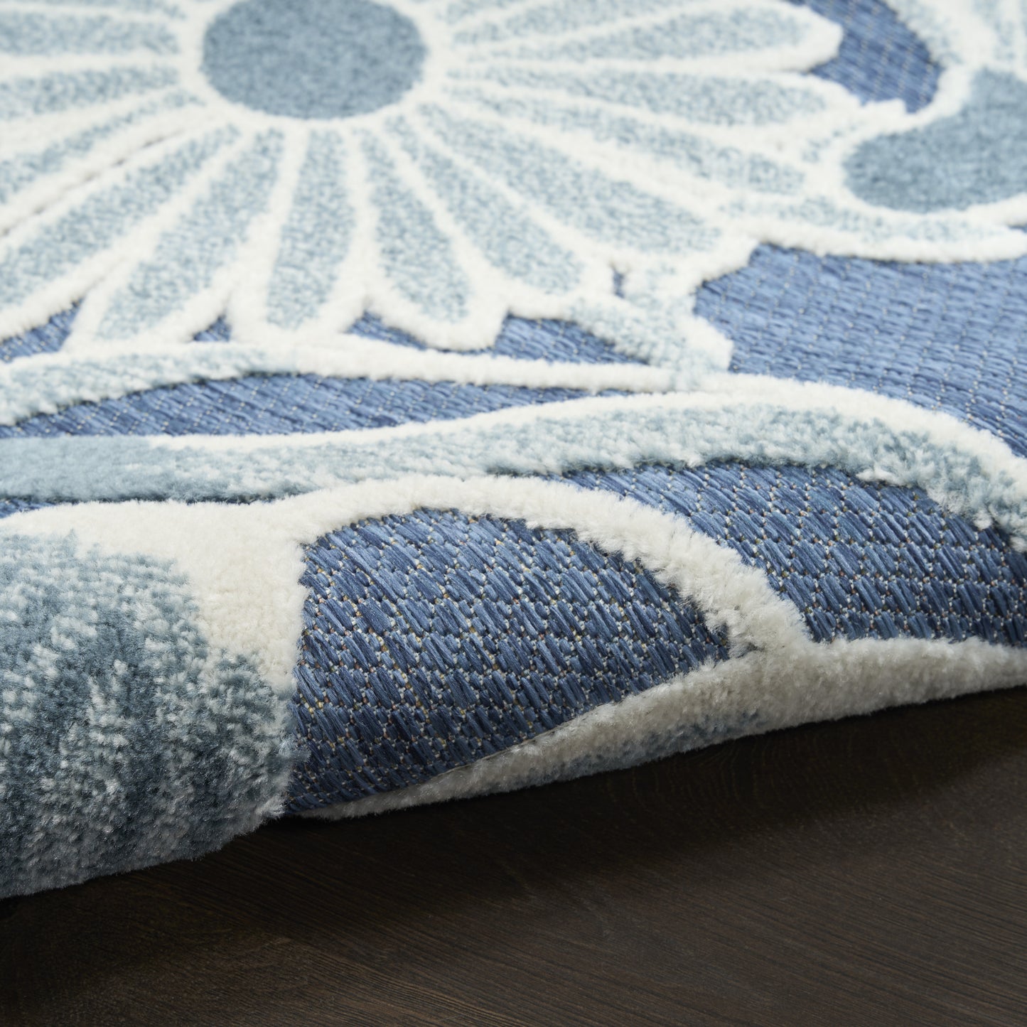 Blue rug with white daisy floral pattern, plush shag pile and light border on dark wood floor.