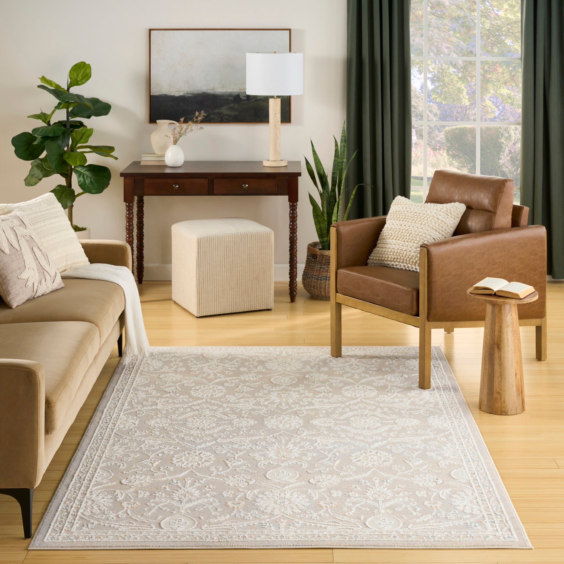 Cozy living room with tan sofa, brown leather chair, gray area rug, wooden console table, plants & green curtains.