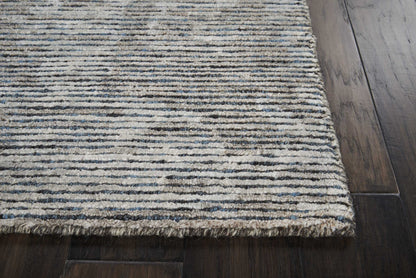 Textured blue-gray striped rug with fringed edge on dark hardwood floor.
