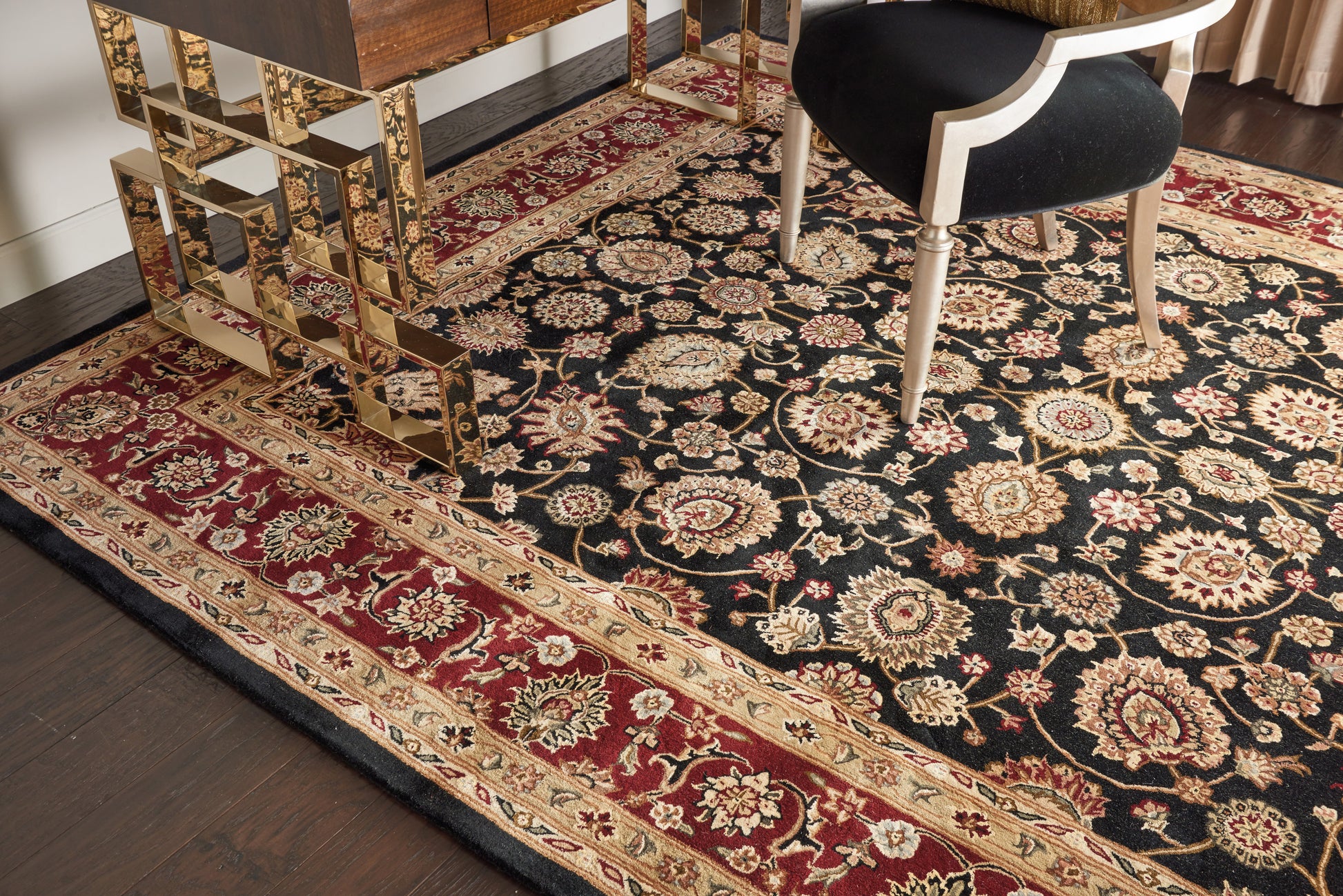 Persian-style oriental area rug with black field, ivory/gold floral motifs and a red border.