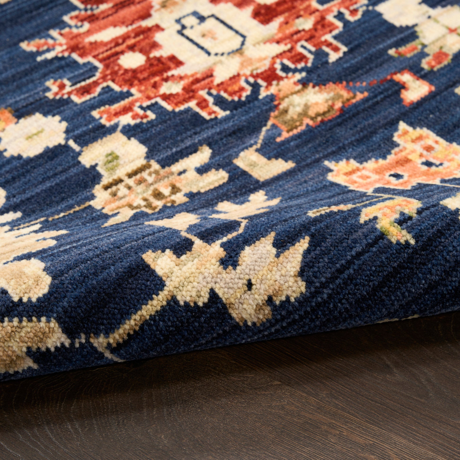Close-up of a navy blue oriental rug with cream, red and beige floral motifs on dark wood floor.