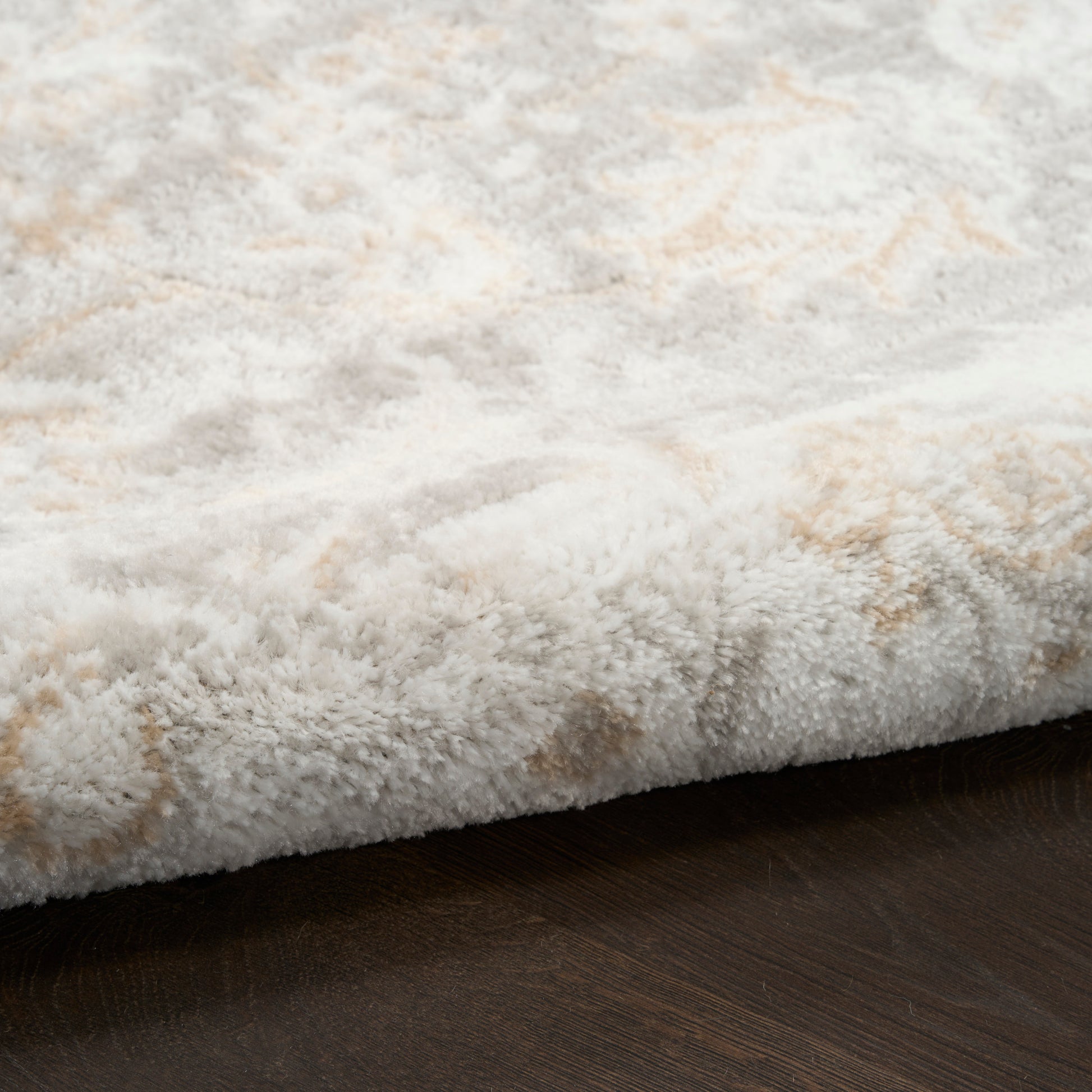 Soft cream shag rug with subtle beige pattern, edge folded over dark wood floor.
