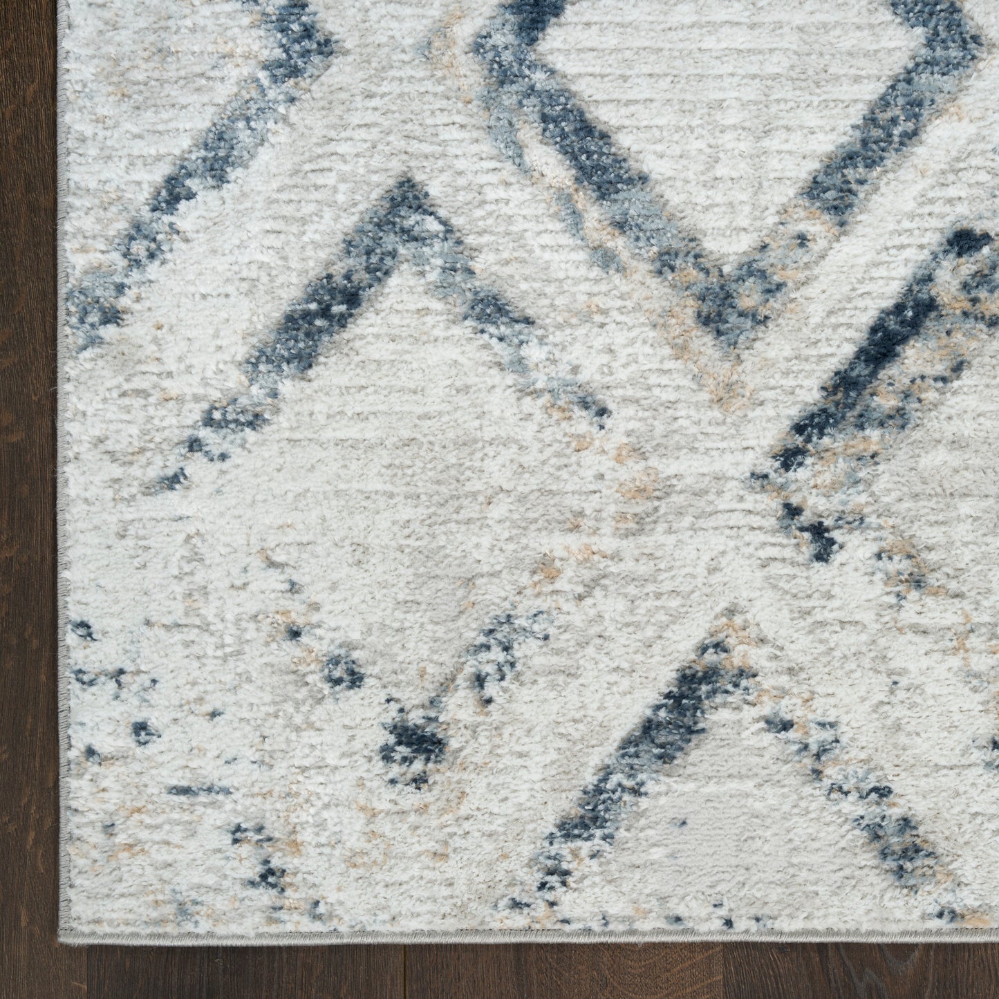 Cream and blue geometric rug with diamond chevron pattern; plush textured pile on dark wood floor.