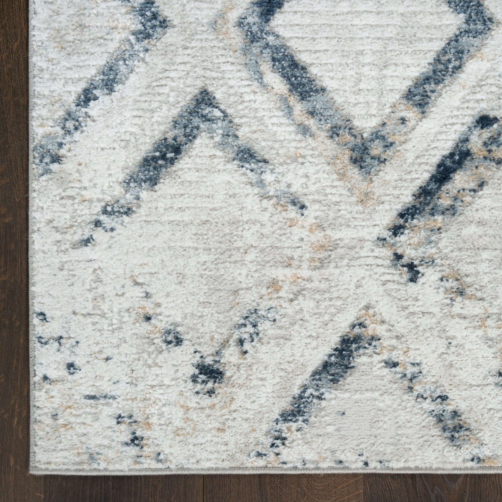 Cream and blue geometric rug with diamond chevron pattern; plush textured pile on dark wood floor.