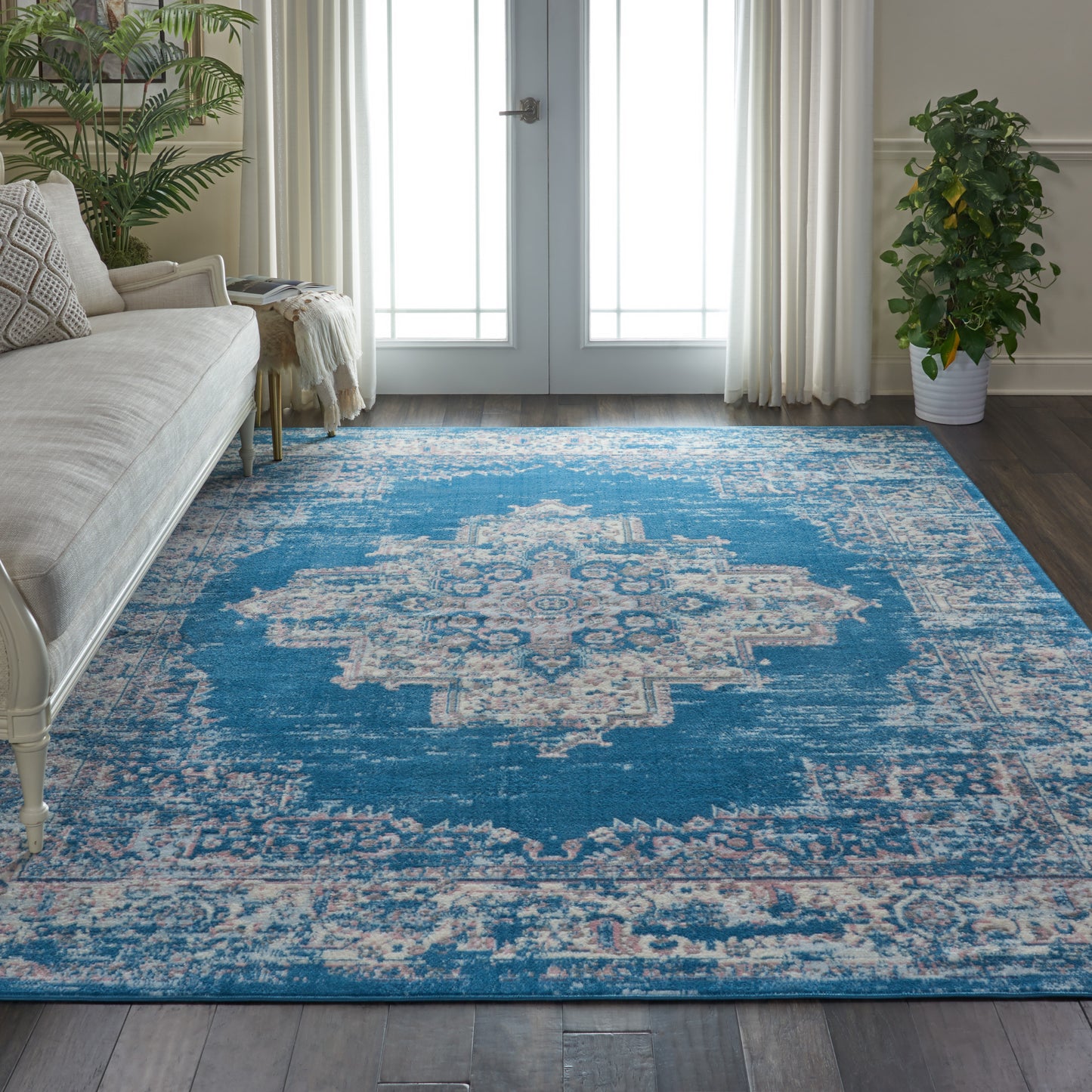 Blue vintage-style area rug with ivory central medallion and distressed border, in a bright living room with cream sofa.