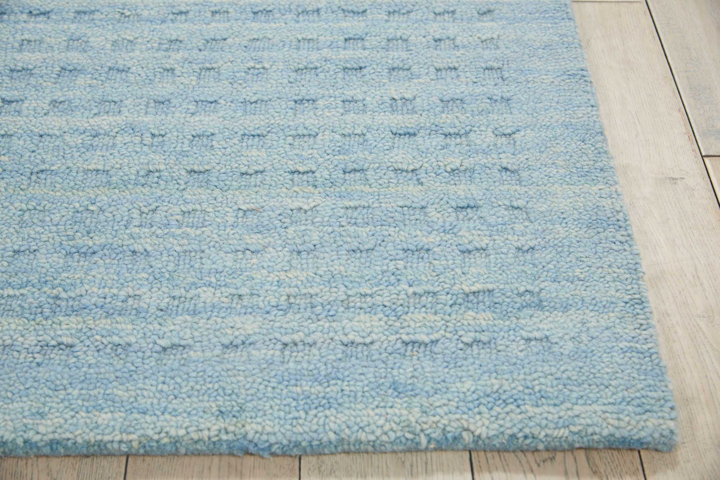Light blue shag rug with cream specks & textured weave on light wood floor.