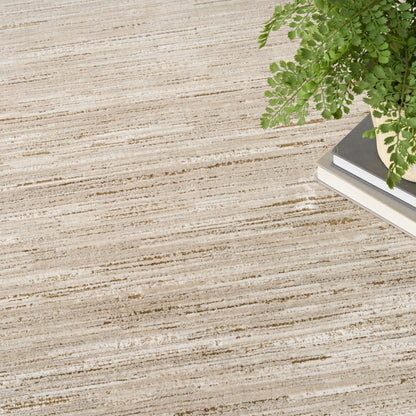 Beige striped area rug with subtle tan lines, placed on a light floor; potted fern and books in corner.