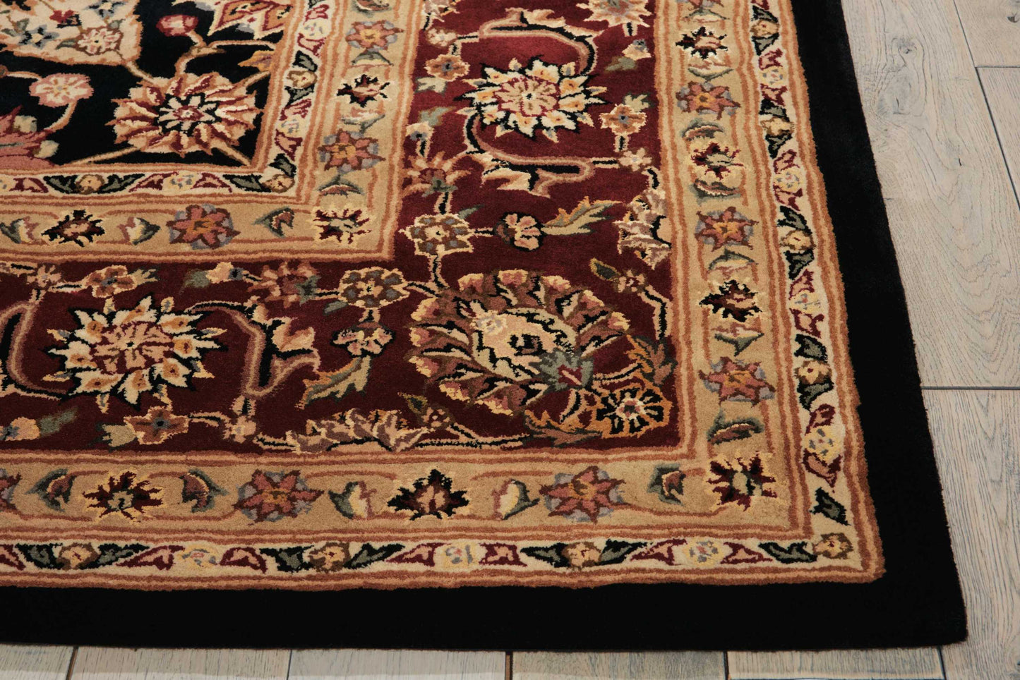 Traditional Persian-style rug on light wood floor; red field with floral medallions, cream and tan border, black outer edge.