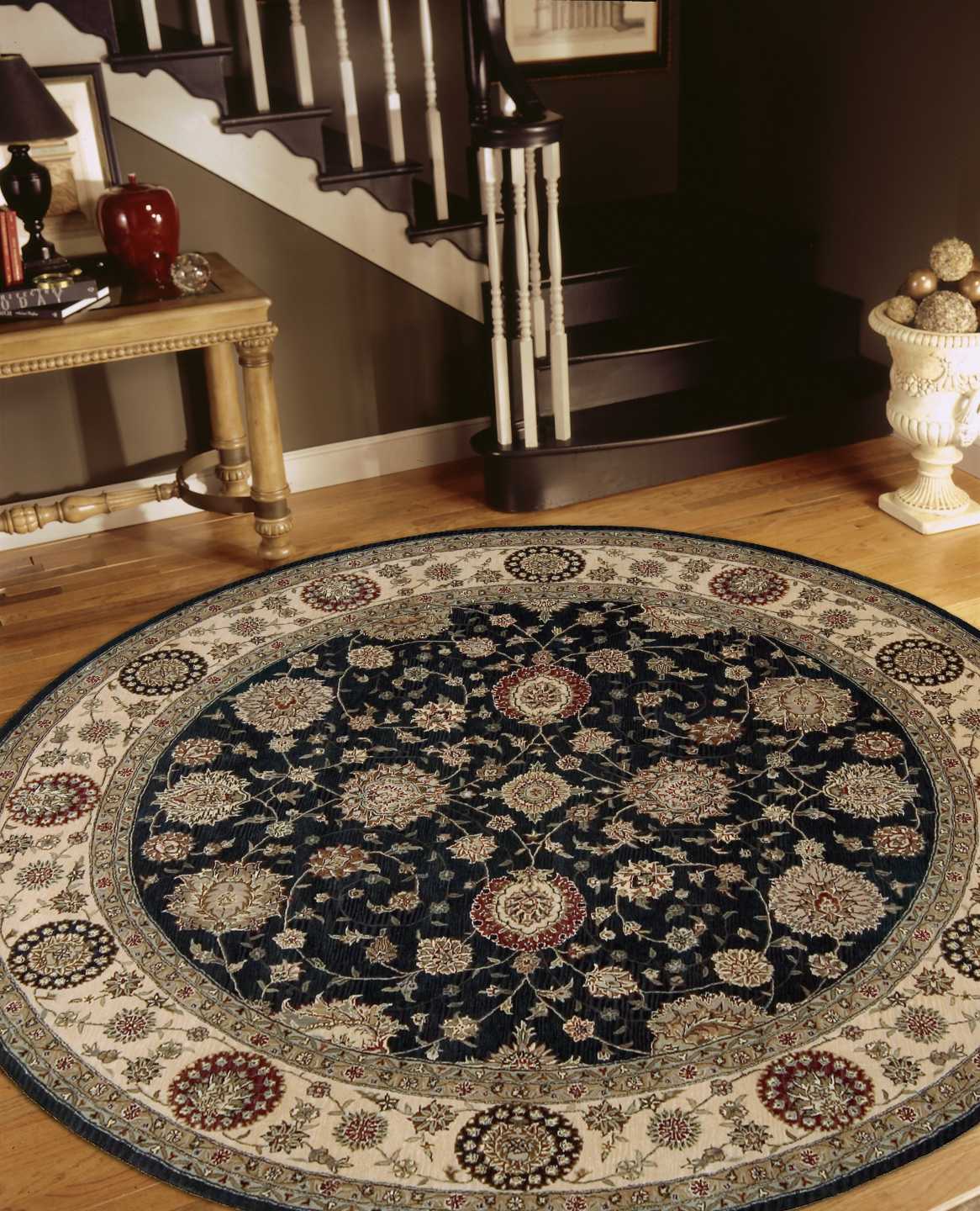 Round oriental area rug with navy center and ivory border of floral medallions; placed in a foyer beside a staircase.
