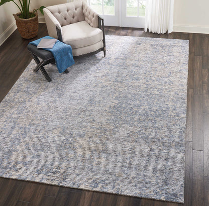 Blue-gray textured rectangular area rug on dark wood floor beside a tufted beige armchair and black ottoman with a blue throw.
