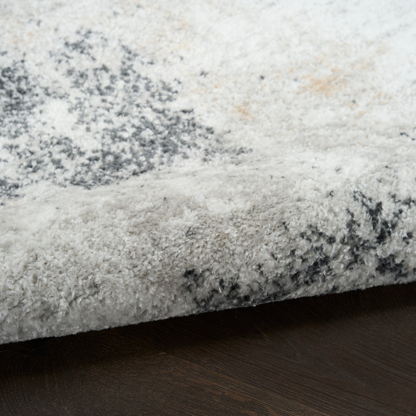 Plush shag rug in ivory-gray with charcoal abstract pattern, edge shown on dark wood floor.