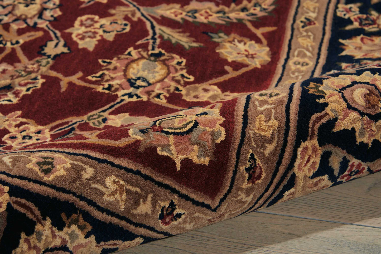 Red oriental rug with cream, gold and navy floral motifs; thick pile, ornate border, laid on a wooden floor.