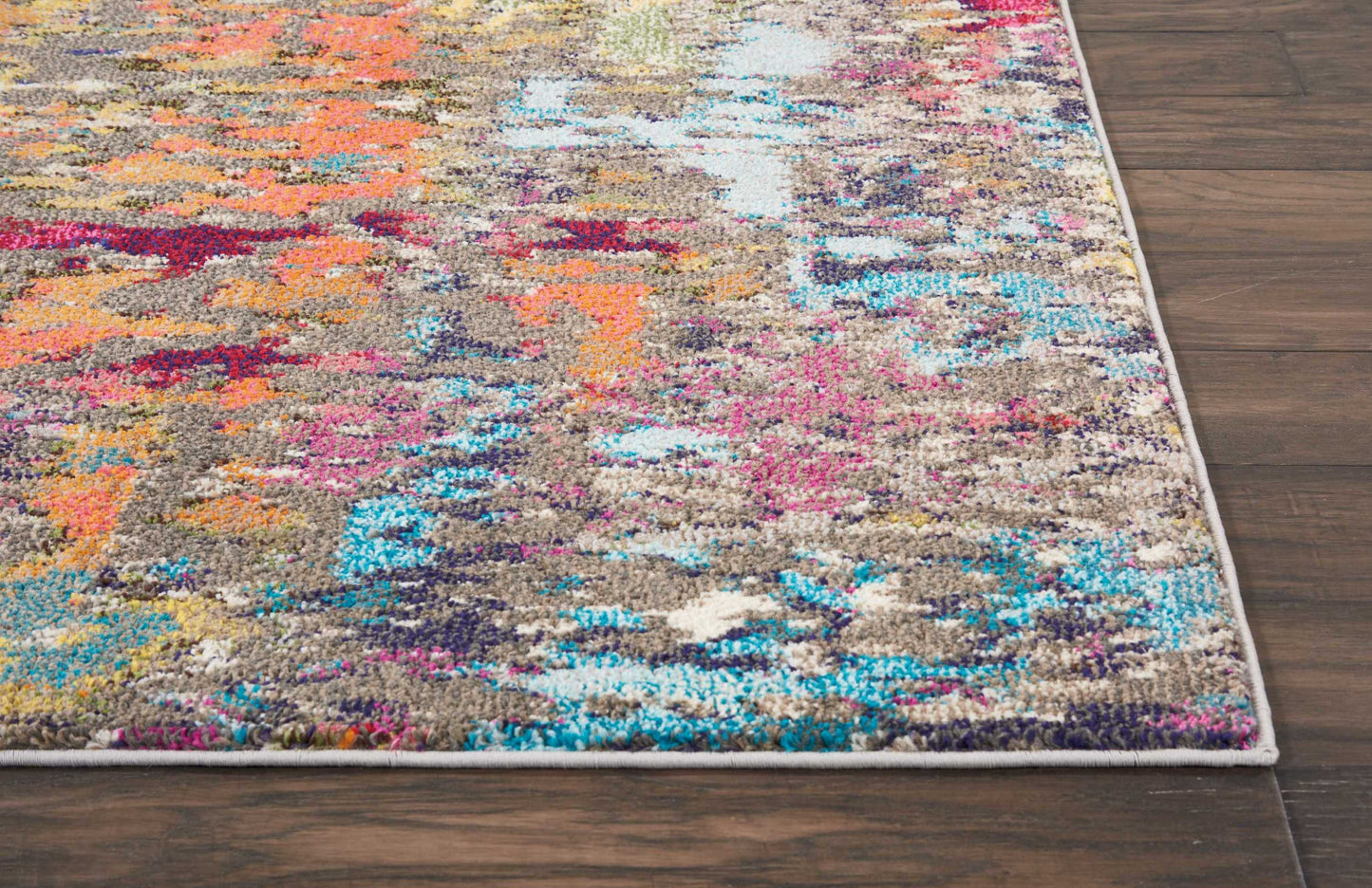 Abstract multicolor area rug with beige base and bright orange, pink and turquoise patches; light edge binding on wood floor.