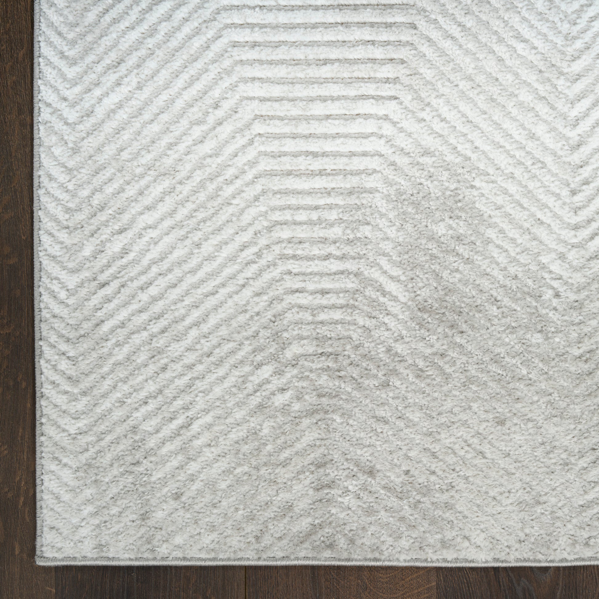 Rectangular light gray plush rug with raised chevron pattern on dark wood floor.