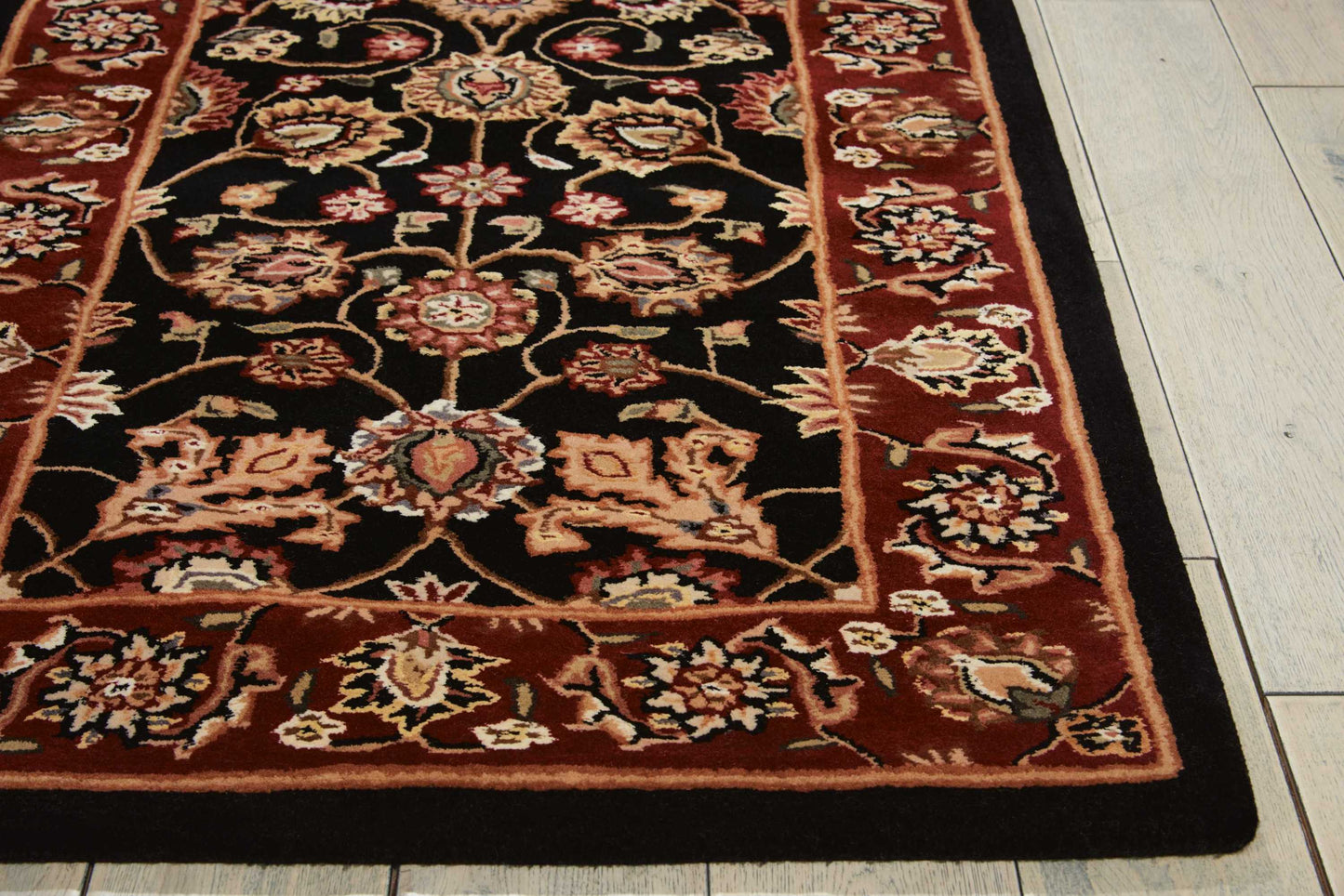 Persian-style rug with black field, red border, ornate cream & rust floral motifs; rectangular on light wood floor.