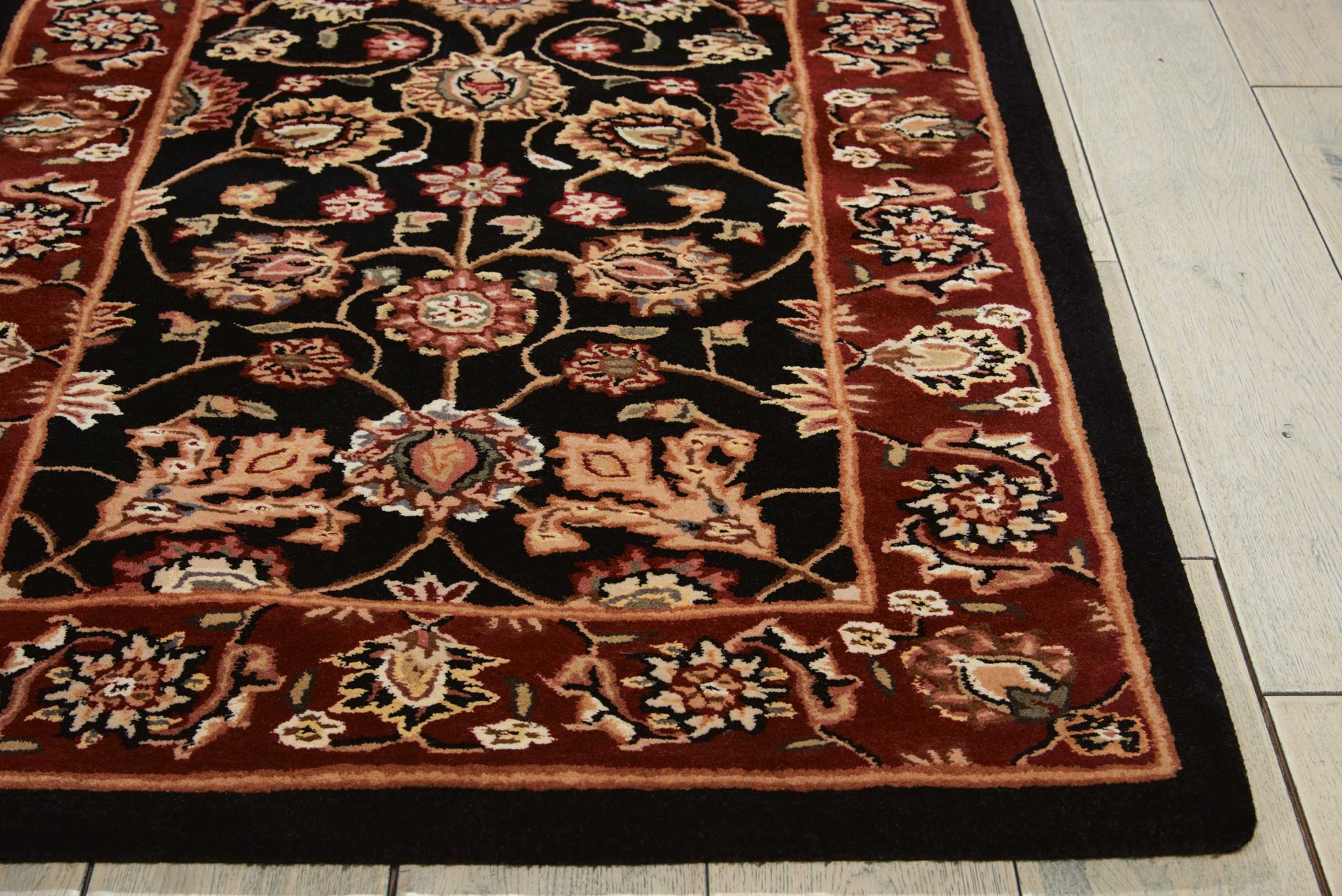 Persian-style rug with black field, red border, ornate cream & rust floral motifs; rectangular on light wood floor.