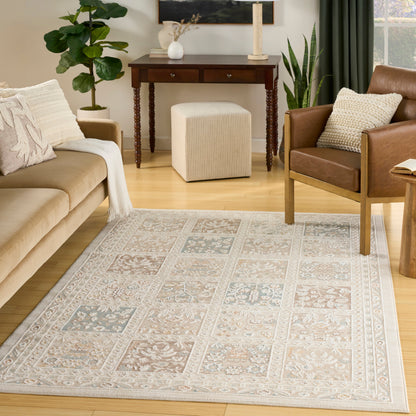 Rectangular beige area rug with pale blue floral panels; cozy living room with tan sofa & leather chair, plants.