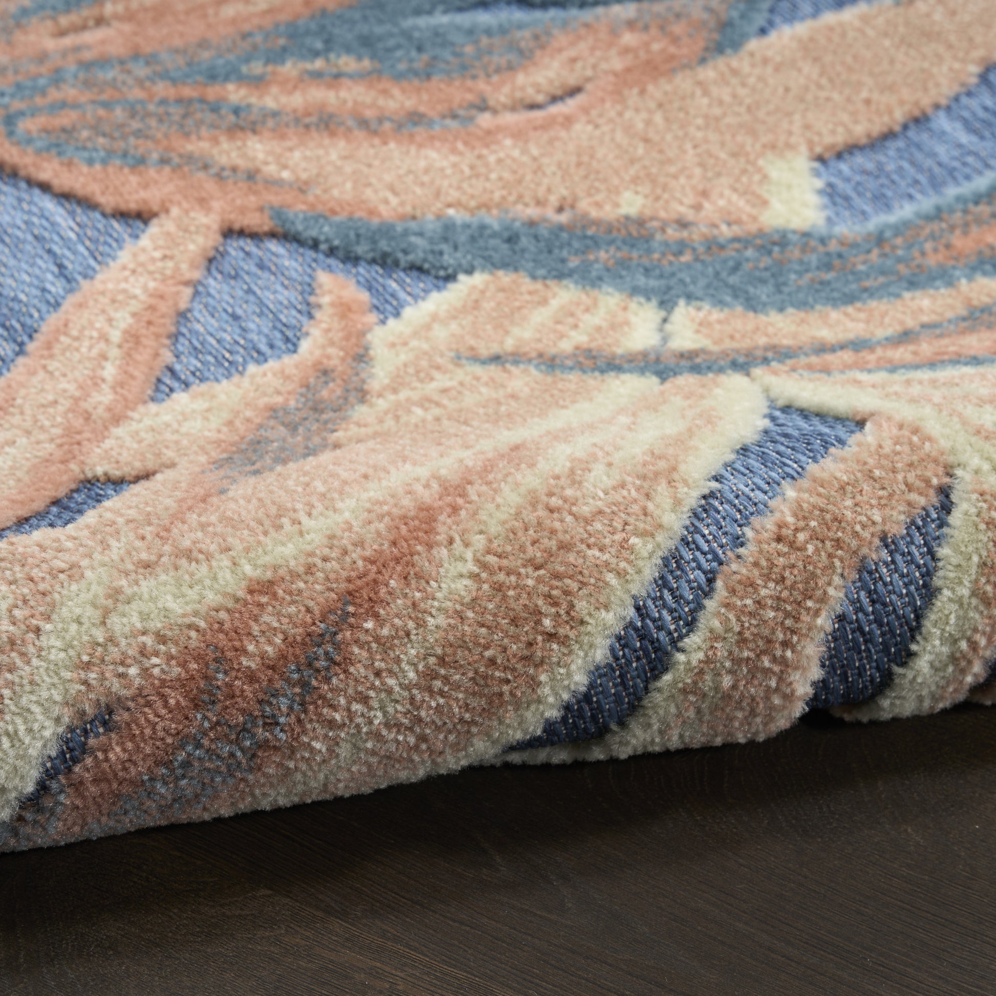 Close-up of plush area rug in pastel peach, cream & blue tones; pile with abstract floral pattern on dark wood floor.