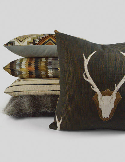 Stacked decorative throw pillows in earth tones; dark brown deer head motif, beige striped, geometric tribal patterns, and faux fur texture.
