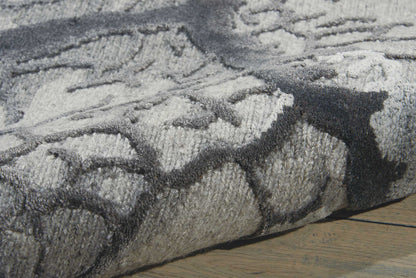 Gray and charcoal geometric patterned plush rug, rolled at edge on a wooden floor.