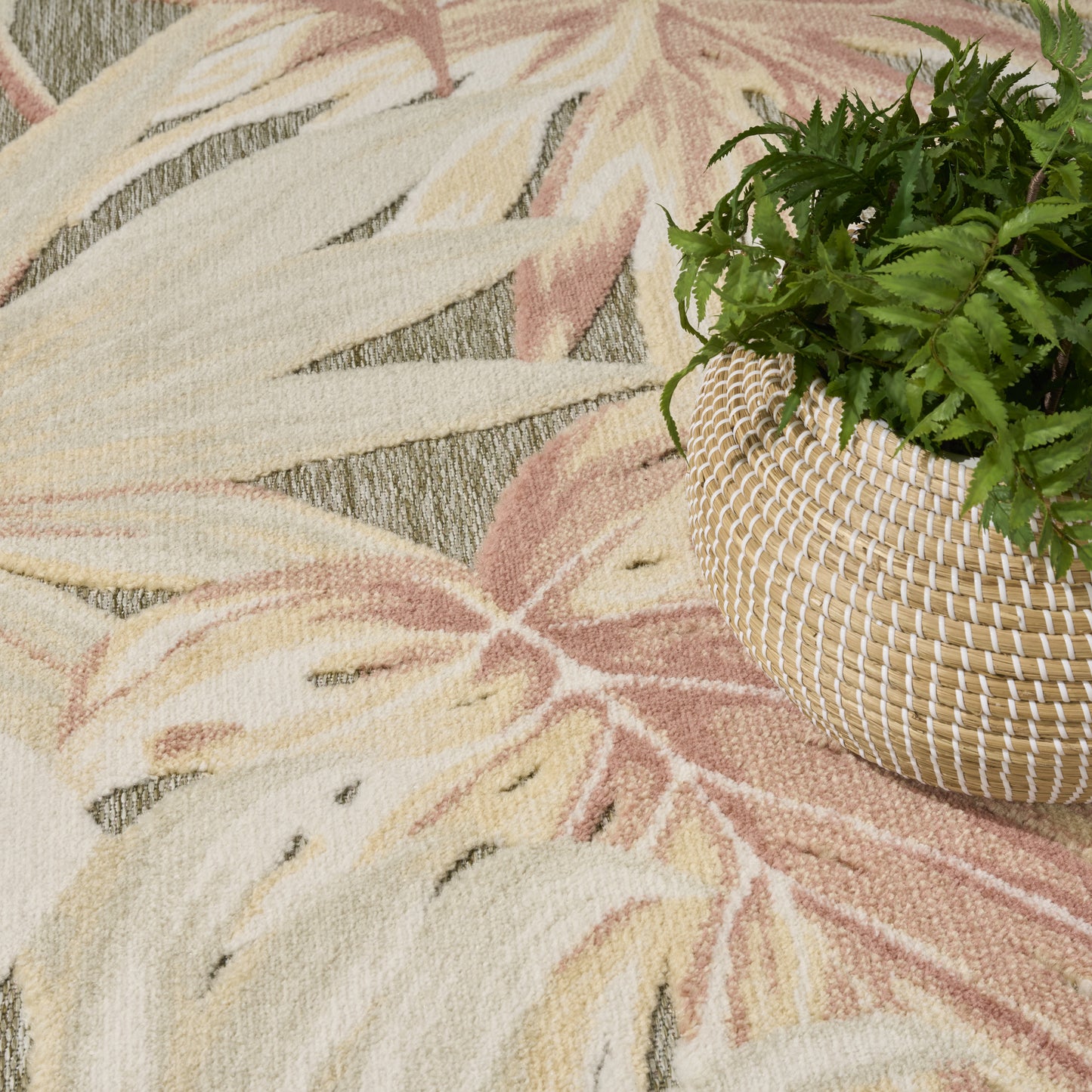 Woven straw basket planter with a lush green fern placed on a pastel tropical leaf rug.