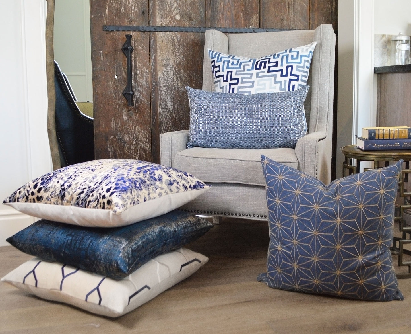 Beige fabric armchair with blue geometric cushions; stacked white and blue pillows on the floor; rustic farmhouse setting.