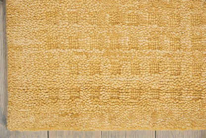 Golden beige shaggy rug with plush pile, rectangular mat on light gray wooden floor.