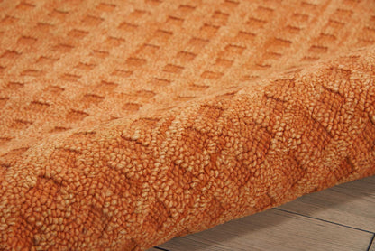 Orange textured rug with tufted geometric pattern and thick shag pile, rolled on a wooden floor.