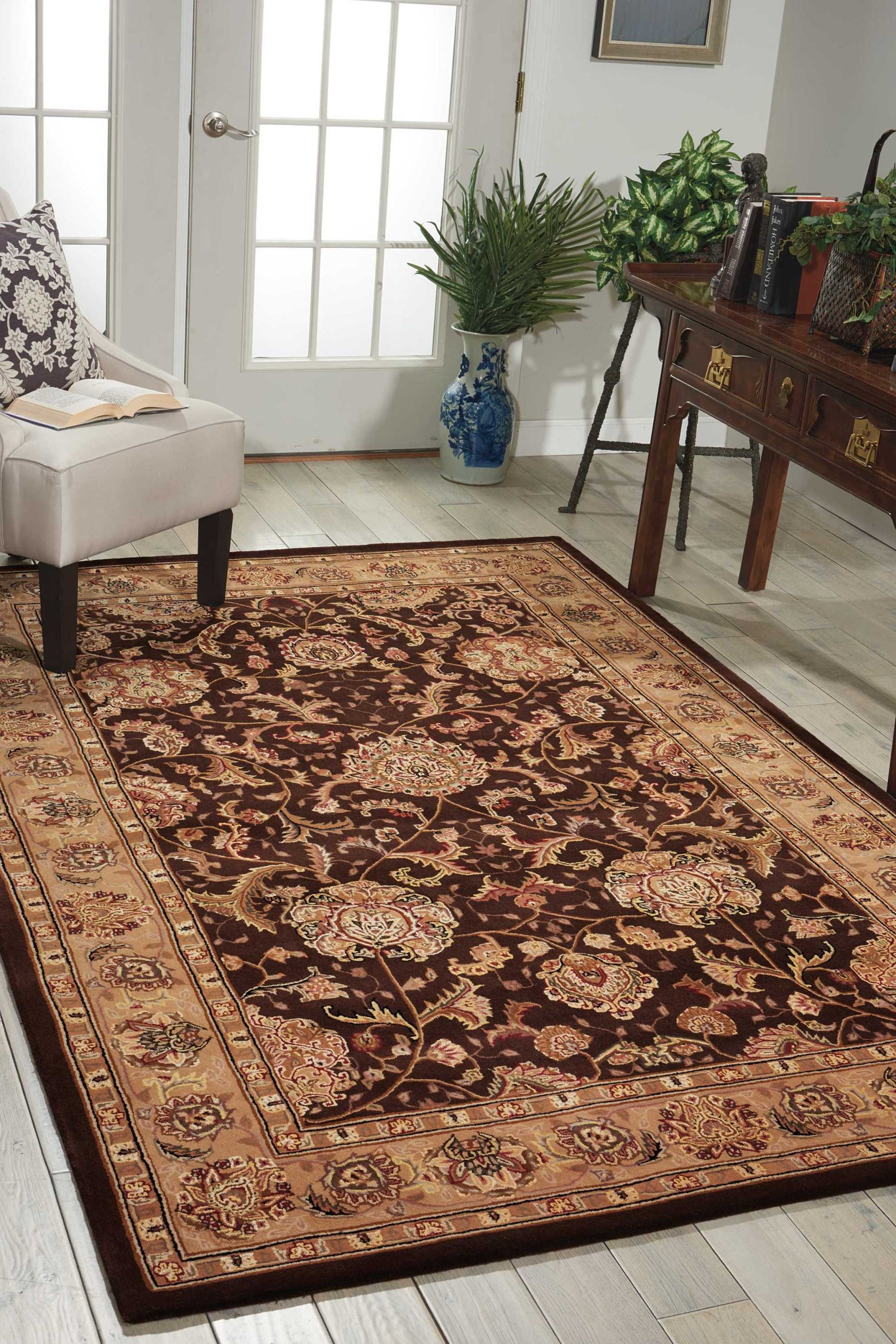 Persian-style burgundy rug with cream border on light wood floor beside a chair and a blue vase near a desk.
