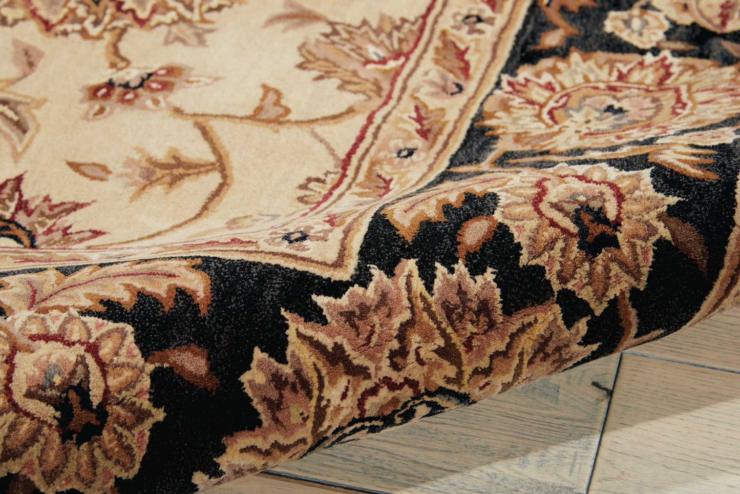 Beige oriental rug with dark border and floral motifs, rolled near edge, on wooden floor.