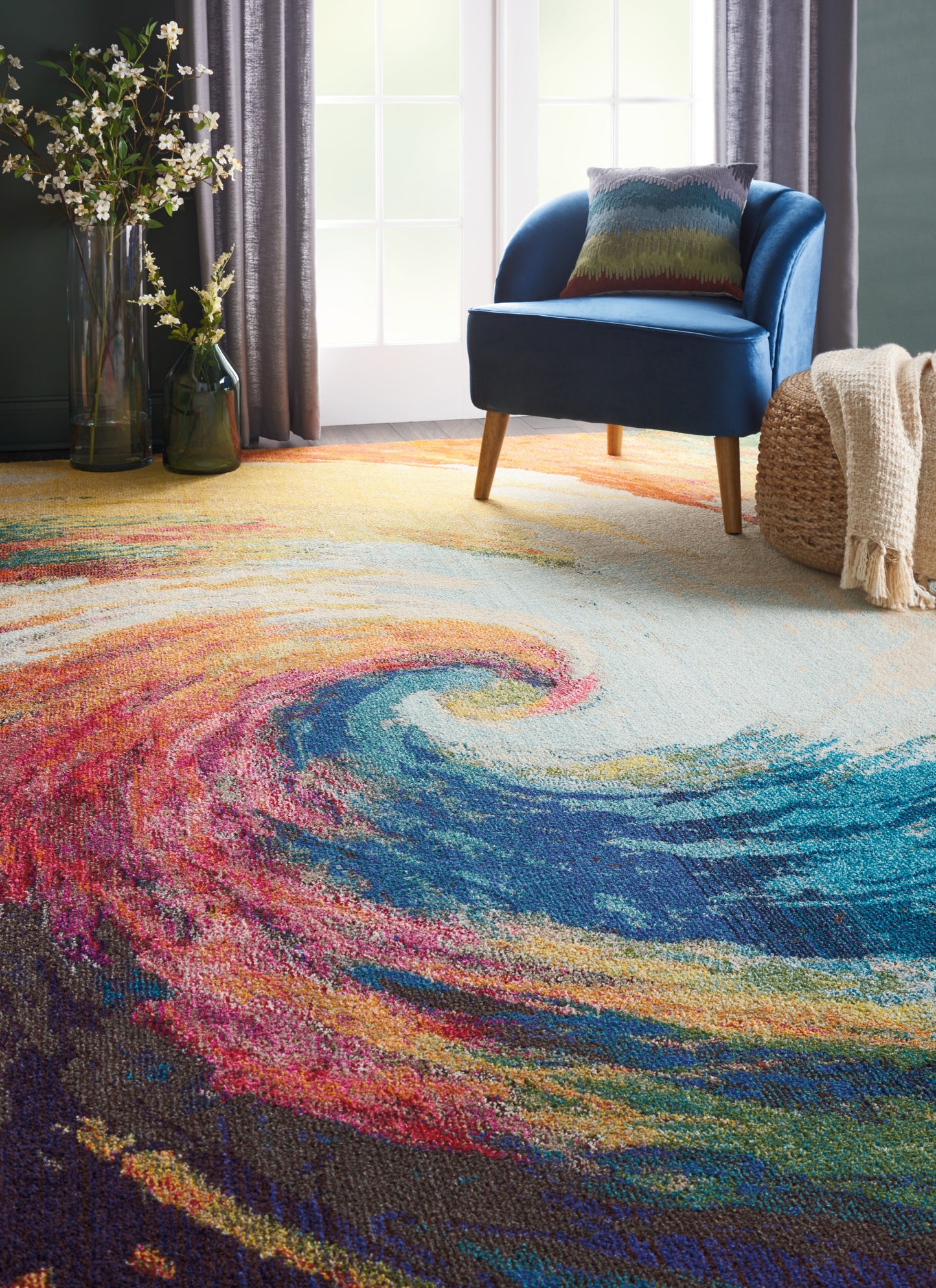 Bright living room with a vivid multicolor swirl rug, blue upholstered chair, and patterned cushion by tall windows.